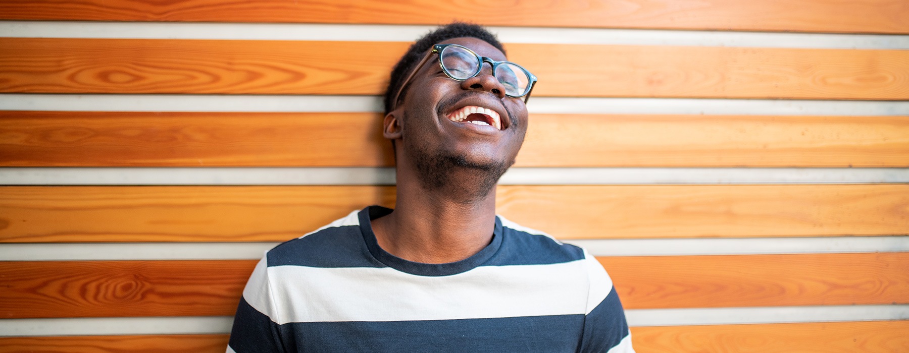 lifestyle image of a man laughing in front of a wooden accented wall